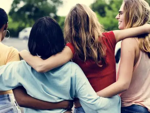 Four young women laugh and walk with their arms around each other