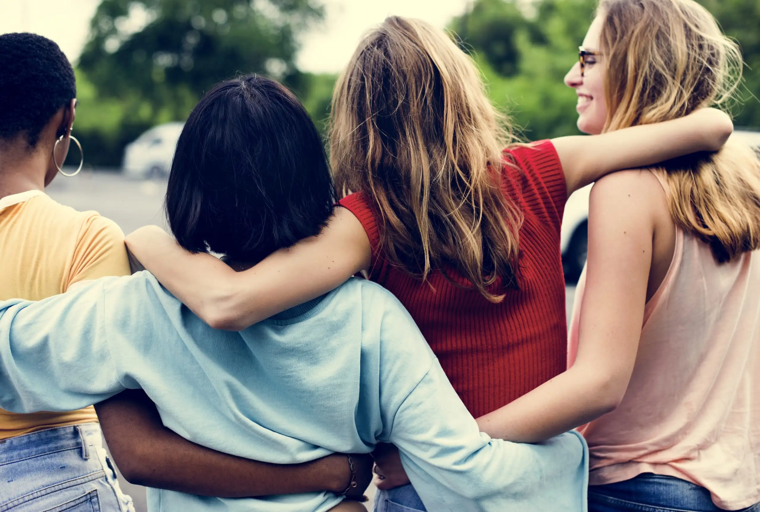 Four young women laugh and walk with their arms around each other