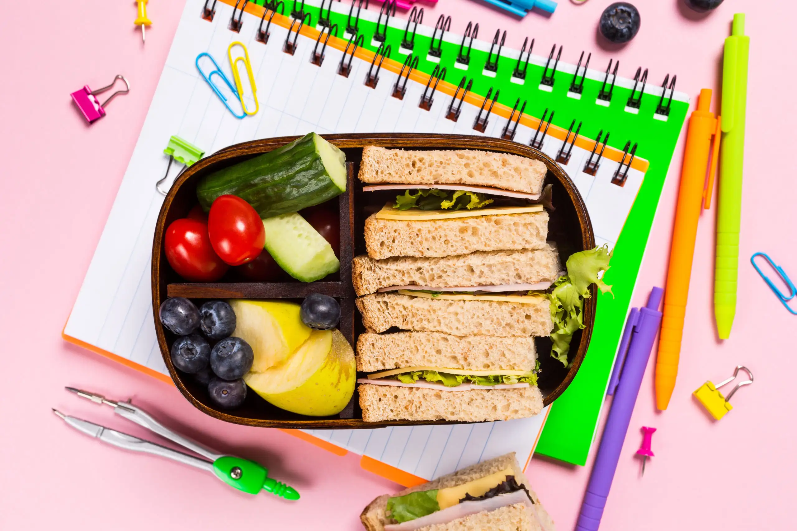 Flat-lay of fully packed school lunch box on top of notebooks and school supplies