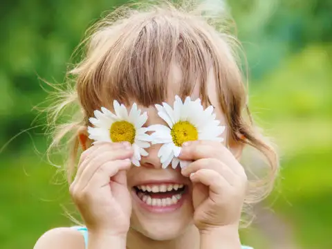 Child holding chamomile flowers in front of her eyes