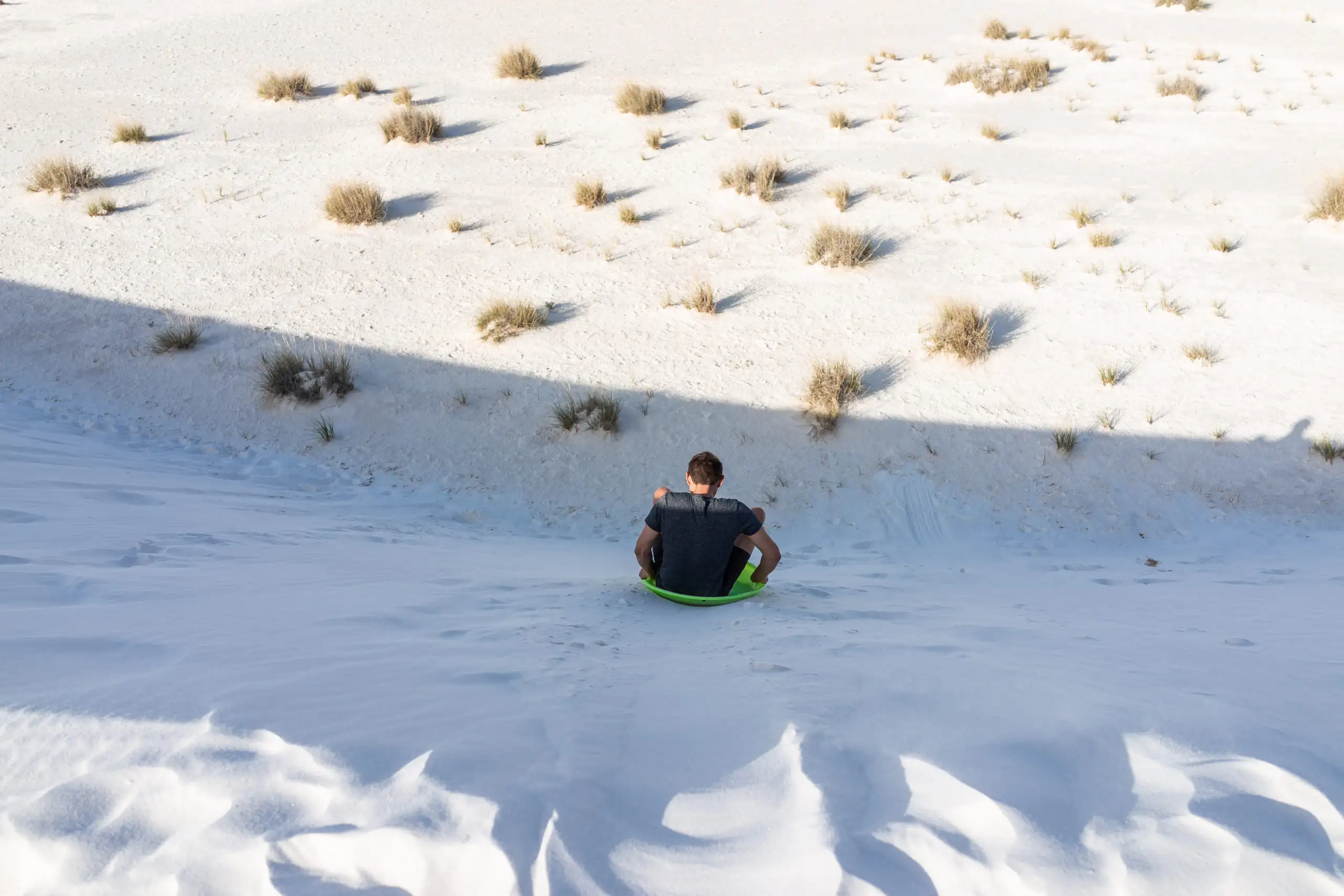 Man sliding down sand dune on sand sled