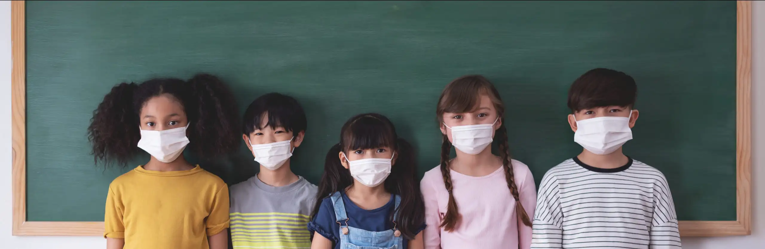 Children in front of a school chalkboard wearing protective face masks