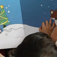 Over-the-shoulder view of three children reading a Christmas storybook