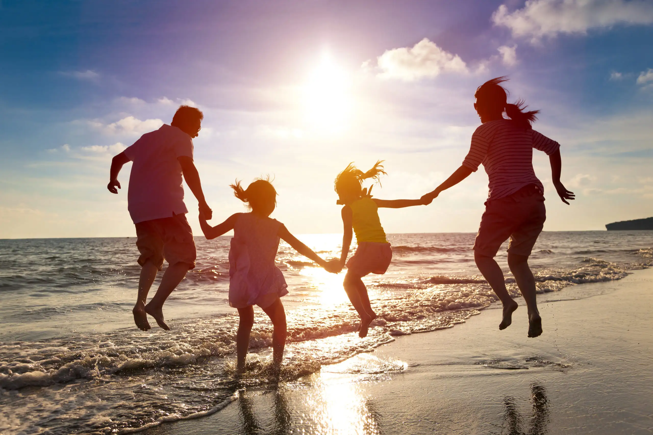 Family jumping together on the beach, backlit by sunset