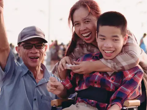 Two parents and a child in a wheelchair on the boardwalk by a beach