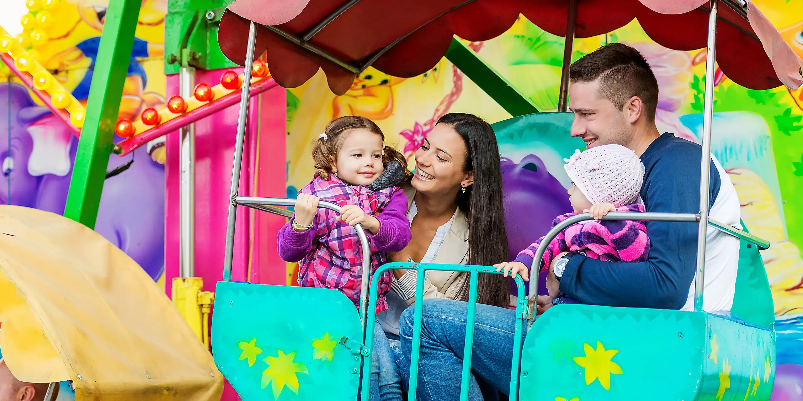 Father, mother, daughters enjoying fun fair ride, amusement park; Courtesy of Halfpoint/Shutterstock