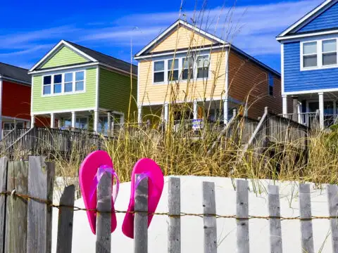 Row of beach rentals on a summer day, pink flip flops on beach fence; Courtesy of StacieStauffSmith Photos/Shutterstock