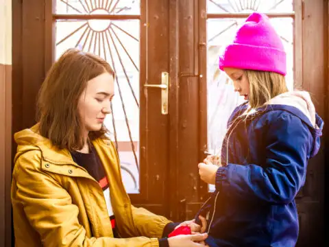 young mother helps her daughter to fasten her jacket next to the front door