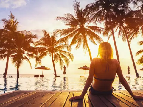 Woman enjoying vacation holidays at luxurious beachfront hotel resort with swimming pool and tropical lansdcape near the beach