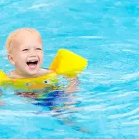 Toddler swimming in pool with swim floaties on; Courtesy of FamVeld/Shutterstock.com